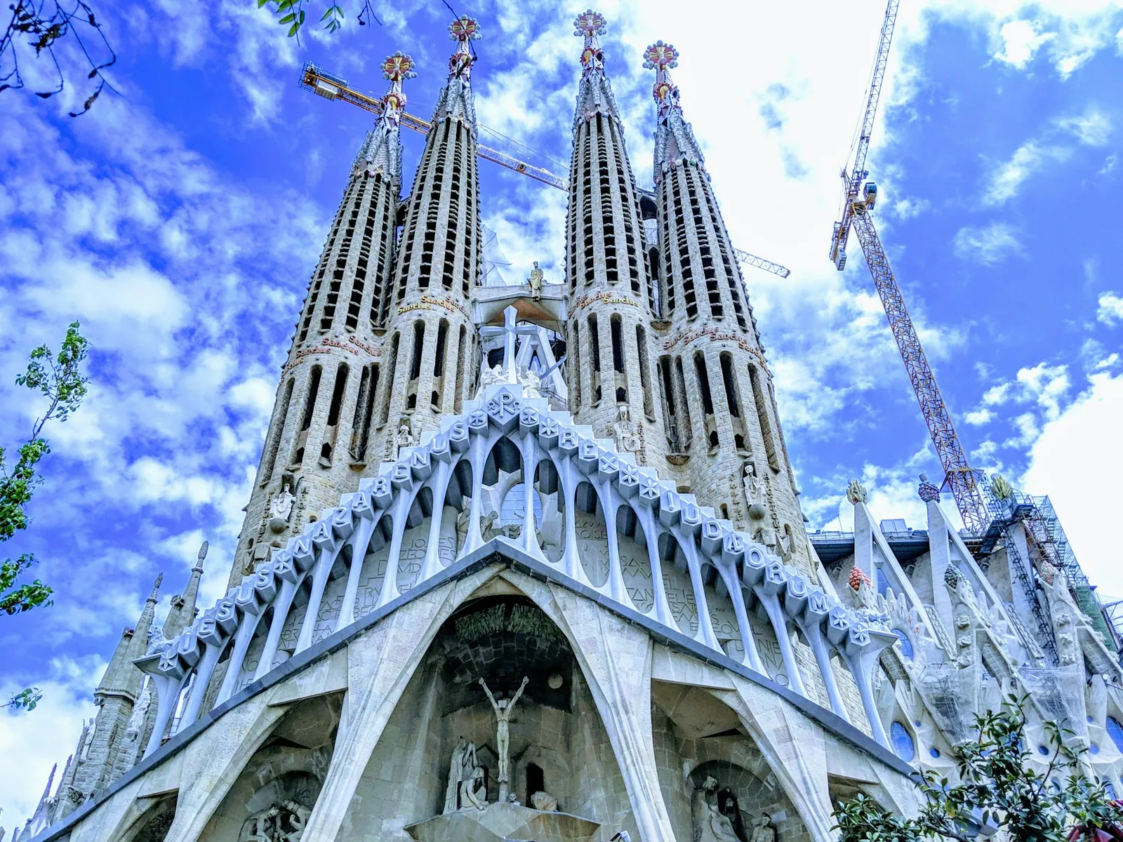 Die Basilika Sagrada Família in Barcelona, ihre verzierten Türme vor blauem Himmel, daneben ragt noch ein Baukran auf